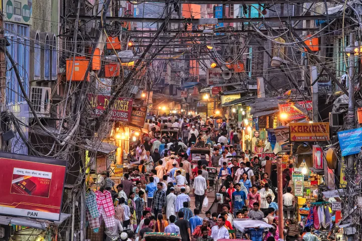 A bustling street scene in Chandni Chowk, Delhi, filled with vibrant shops, tangled overhead wires, and a dense crowd of people exploring the market.