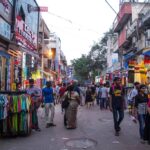 Busy street scene at Sarojini Nagar Market in Delhi with colorful clothes on display, bustling shoppers, and vibrant roadside shops during the evening