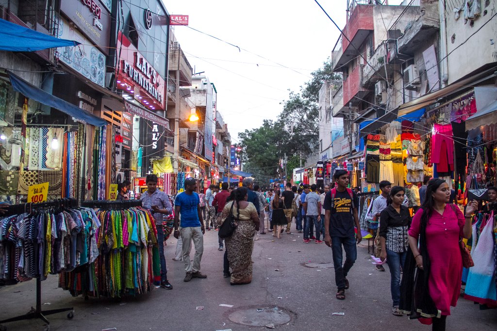 Busy street scene at Sarojini Nagar Market in Delhi with colorful clothes on display, bustling shoppers, and vibrant roadside shops during the evening