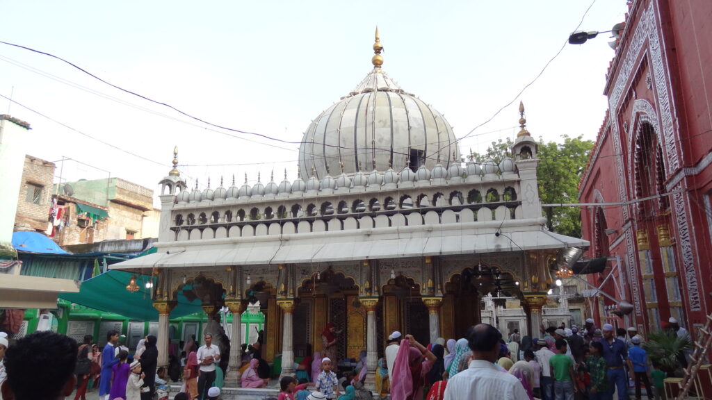 Devotees gathered at the Nizamuddin Dargah in Delhi, showcasing the white marble dome and intricate Mughal-style architecture of the shrine.