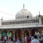 Devotees gathered at the Nizamuddin Dargah in Delhi, showcasing the white marble dome and intricate Mughal-style architecture of the shrine.