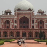 Front view of Humayun’s Tomb in Delhi showcasing its grand Mughal architecture with red sandstone arches, white marble dome, and lush green gardens.