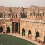 Ruins of Tughlaqabad Fort, Delhi, featuring massive stone walls, arched gateways, and rugged landscape under a bright blue sky.