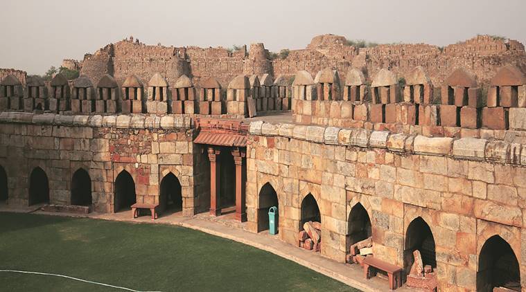 Ruins of Tughlaqabad Fort, Delhi, featuring massive stone walls, arched gateways, and rugged landscape under a bright blue sky.